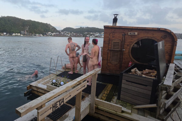 Mennesker utenfor badstu, med badende i Gandsfjorden