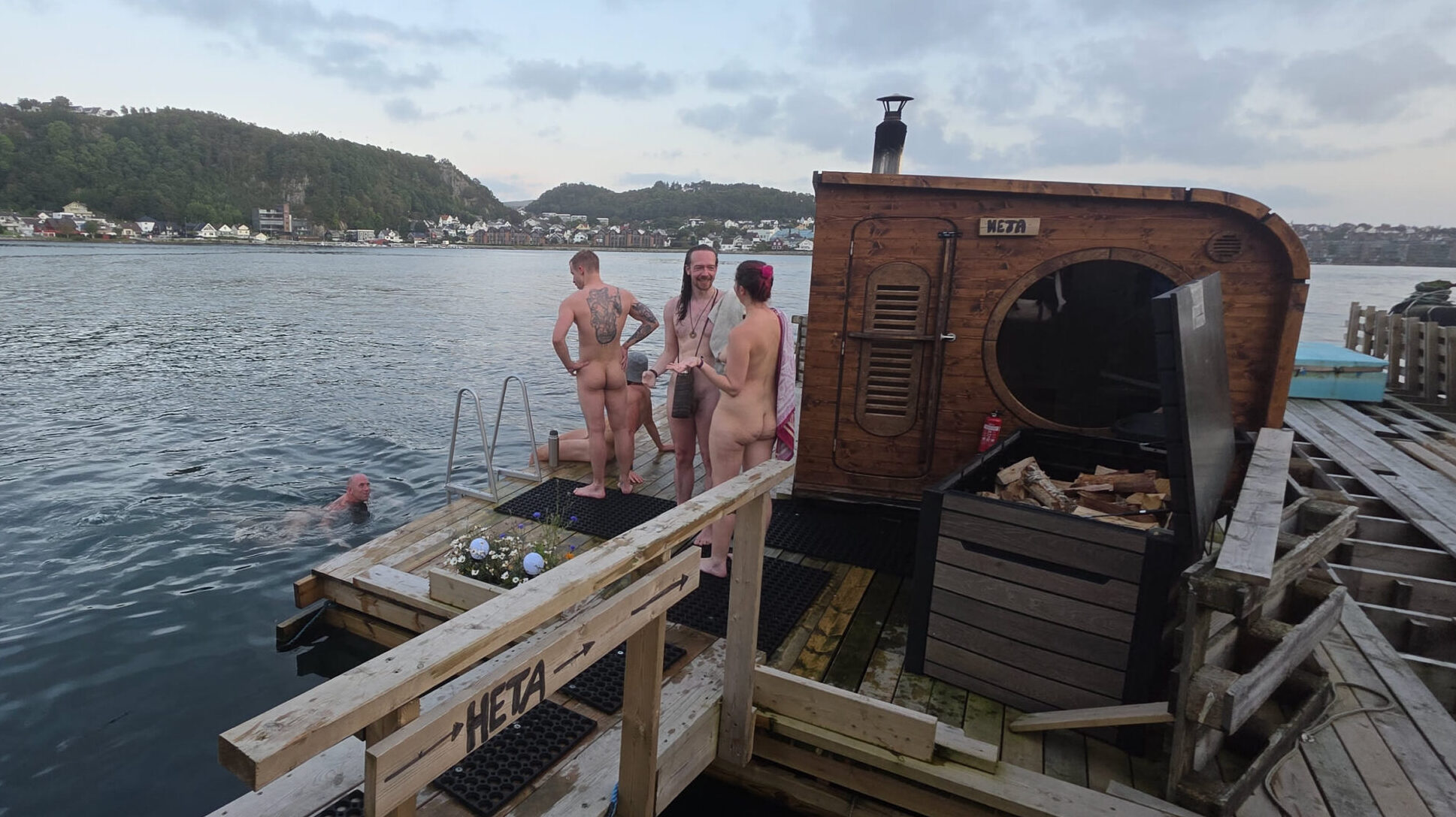 Mennesker utenfor badstu, med badende i Gandsfjorden