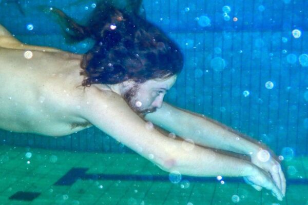Naken mann svømmer under vannet