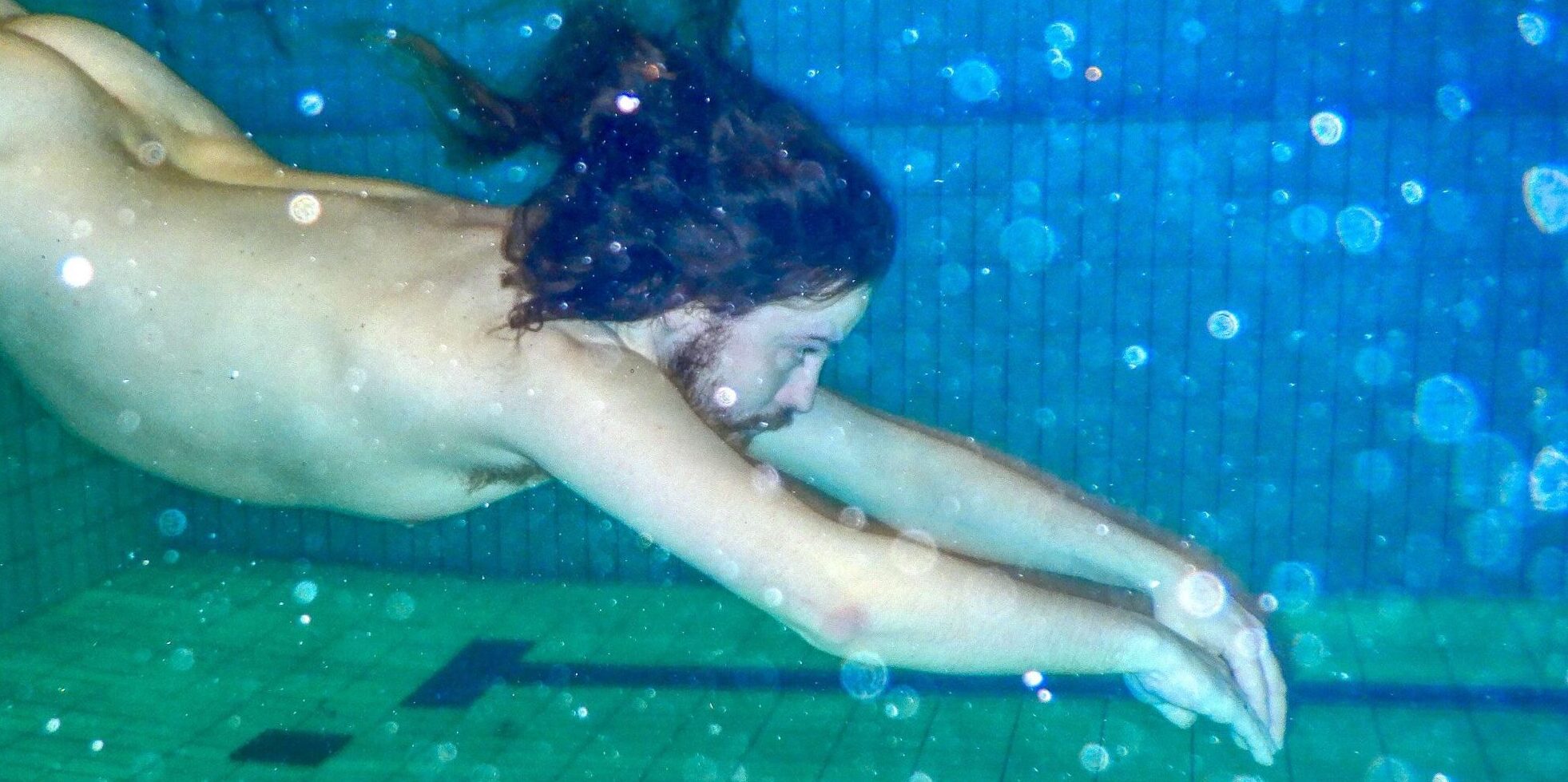 Naken mann svømmer under vannet