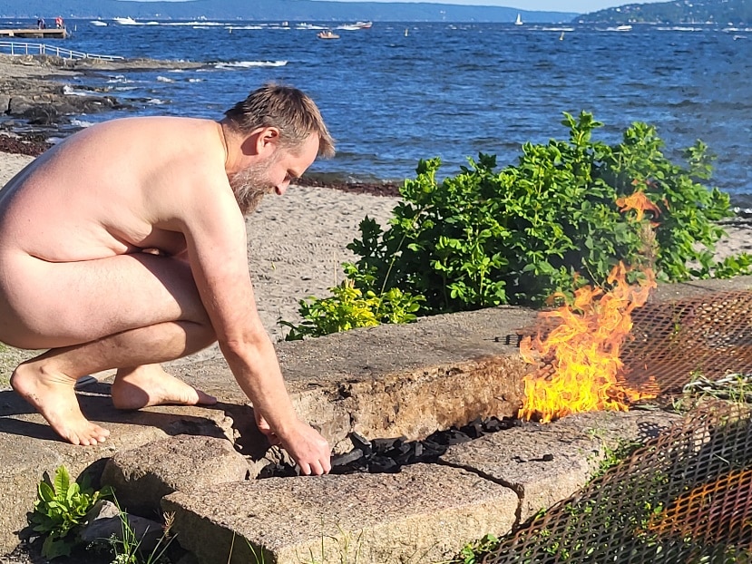 Naken mann tenner bål på fellesgrillen på Huk